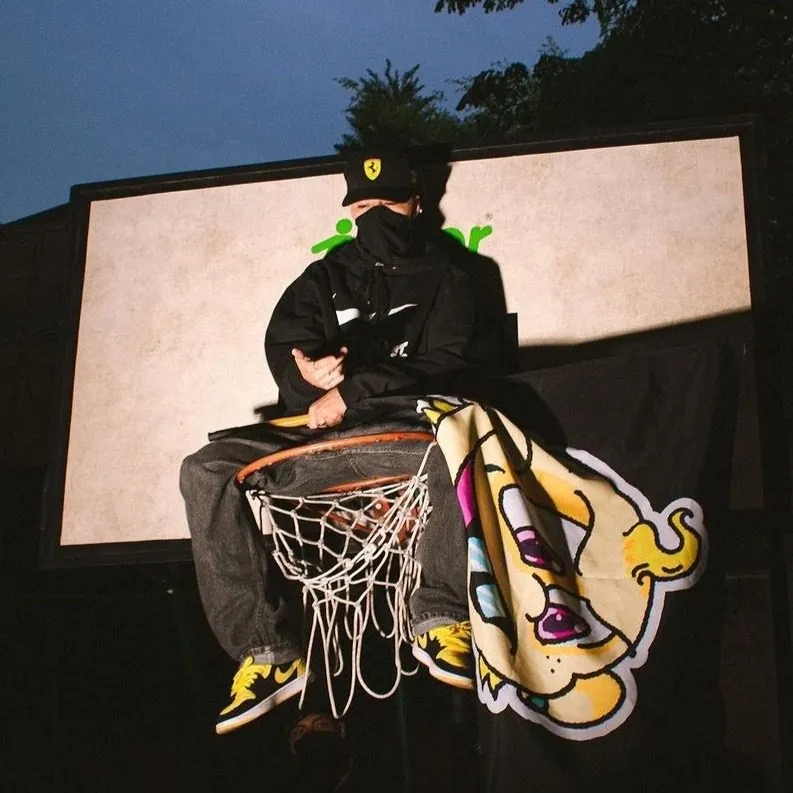 Mainyy sentado en un aro de baloncesto de noche, estilo callejero